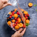 Fresh summer fruits and berries, apricots, blueberries, strawberries in colander, washing fruits and berries, woman`s hands, wate