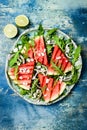 Fresh summer grilled watermelon salad with feta cheese, arugula, onions on blue background.
