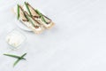Fresh summer healthy appetizer of whole grain crisps breads with sprats preserves, green onion, cream cheese on white wood board.