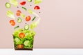 Fresh summer salad of raw vegetable with flying ingredients - tomatoes, cucumber and green salad above craft box for take away. Royalty Free Stock Photo