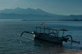 Fresh sunny morning on tropical beach with sun glares on water, tradition fishing boat on shore, foggy blue mountains on horizon. Royalty Free Stock Photo