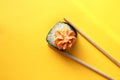 Fresh sushi roll, isolated on a yellow background. One sushi rolls are between the chopsticks. Asian cuisine. Copy space Royalty Free Stock Photo