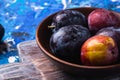 Fresh sweet plum fruits in brown wooden bowl on old cutting board, blue abstract background