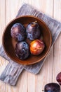 Fresh sweet plum fruits in brown wooden bowl on old cutting board, wood table background Royalty Free Stock Photo