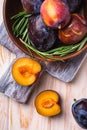 Fresh sweet plum fruits whole and sliced in brown wooden bowl with rosemary leaves on old cutting board Royalty Free Stock Photo