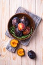 Fresh sweet plum fruits whole and sliced in brown wooden bowl with rosemary leaves on old cutting board, wood table background Royalty Free Stock Photo