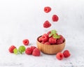 Fresh sweet raspberry falling into wooden bowl with berries and mint leaves on light stone background Royalty Free Stock Photo