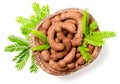 Fresh tamarind fruits and leaves in the wooden bowl, isolated on the white background, top view