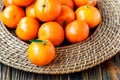 Fresh tangerines with leaves on wicker plate over old wooden table