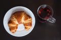 Fresh and tasty bavarian croissant on white plate and a glass of fruit tea over wooden background