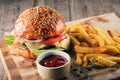 Fresh tasty burger and french fries with sauce on wooden cutting board with wood background Royalty Free Stock Photo