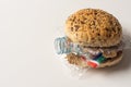 Fresh tasty burger with plastic waste and paper cardboard inside on white background. Recycled waste in our food concept Royalty Free Stock Photo