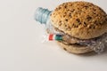 Fresh tasty burger with plastic waste and paper cardboard inside on white background. Recycled waste in our food concept