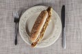 Fresh tasty hot dog with fried onions and fresh lettuce with mustard on a porcelain plate with fork and knife Royalty Free Stock Photo