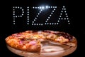 Fresh tasty Italian pizza on a black background with a spectacular light inscription `pizza`