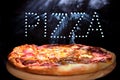 Fresh tasty Italian pizza on a black background with a spectacular light inscription `pizza` and smoke.