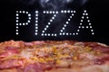 Fresh tasty Italian pizza on a black background with a spectacular light inscription `pizza` and smoke.