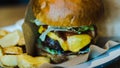 Fresh, tasty, juicy hamburger with cheese, tomatoes, seasoned marbled beef, fresh salad and potatoes on a wooden table. Side view