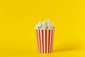 Fresh tasty popcorn and red cup on color yellow background, side view with space for text. Cinema snack
