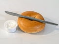 Fresh toasted bagel with a knife and cream cheese on a white background.