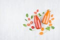 Fresh tomato and carrot juices in glass bottles with ingredients and green spinach leaves on white wood board, mock up for design.