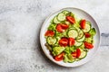 Fresh tomato and cucumber salad in white bowl, gray background. Healthy food concept