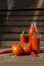 Fresh tomatoes on a branch ,2 cups tomato juice with a sprig of mint, a bottle of tomato juice, chili, spices on a brown wooden