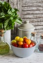 Fresh tomatoes in a ceramic bowl, green garden herb, olive oil and spices on a light rustic wood background.