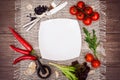 Fresh tomatoes, chili pepper and other spices and herbs around modern white square plate in the center of wooden table and cloth Royalty Free Stock Photo