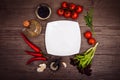 Fresh tomatoes, chili pepper and other spices and herbs around modern white square plate in the center of wooden table and cloth Royalty Free Stock Photo