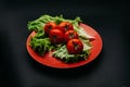 Fresh tomatoes with drops of water and lettuce on a red plate on a dark background Royalty Free Stock Photo