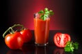 Fresh tomatoes and a glass full of tomato juice. Tomatoes and parsley lie on a black reflective table with a dark background and Royalty Free Stock Photo
