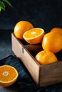 Fresh tropical fruits in a wooden delivery box on dark stone background. Sweet juicy oranges in wooden basket, side view, close up Royalty Free Stock Photo