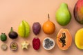 Fresh tropical whole and halved fruits on a beige background making a row.