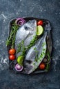 Fresh uncooked Dorado fish or sea bream with ingredients for cooking on dark background