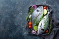 Fresh uncooked Dorado fish or sea bream with ingredients for cooking on dark background