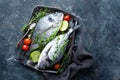 Fresh uncooked Dorado fish or sea bream with ingredients for cooking on dark background