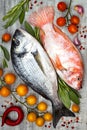 Fresh uncooked dorado or sea bream and red tilapia fish with lemon, aromatic herbs, vegetables and spices over grey background