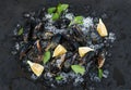 Fresh uncooked mussels with lemon, herbs and spices on chipped ice over dark slate stone backdrop Royalty Free Stock Photo