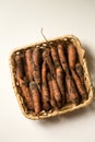 Unwashed carrots in a square basket on a white background