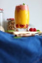 Fresh vegan layered dessert in a glass of colored smoothies of mango and banana with raspberries ice cream.