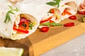 Fresh vegan tortilla wraps with bell pepper, tomato and cucumber on wooden cutting board with lime and chili pepper.