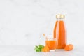 Fresh vegetable orange carrot juice in glass bottle mock up with glass, straw, green parsley, slices in soft light white interior.