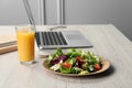 Fresh vegetable salad, glass of juice and laptop on white wooden table at workplace. Business lunch