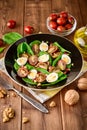 Fresh vegetable salad with spinach, cherry tomatoes, quail eggs, pomegranate seeds and walnuts in black plate on wooden table. Royalty Free Stock Photo