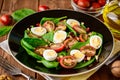 Fresh vegetable salad with spinach, cherry tomatoes, quail eggs, pomegranate seeds and walnuts in black plate on wooden table. Royalty Free Stock Photo