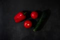 Fresh vegetables on black kitchen table. Minimalistic restaurant menu. Whole wet red bell pepper, two tomatoes and green cucumber Royalty Free Stock Photo
