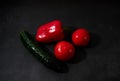 Fresh vegetables on black kitchen table. Minimalistic restaurant menu. Whole wet red bell pepper, two tomatoes and green cucumber Royalty Free Stock Photo