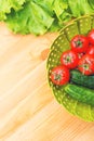 Fresh vegetables cucumbers and tomatoes in a green bowl on a wooden table next to green lettuce leaves. Top view of a Royalty Free Stock Photo