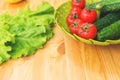 Fresh vegetables cucumbers and tomatoes in a green bowl on a wooden table next to green lettuce leaves. Vegetarian diet Royalty Free Stock Photo